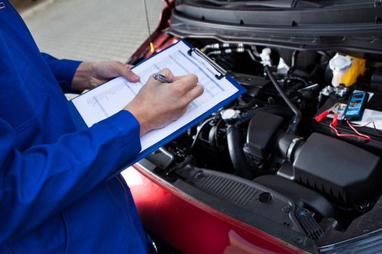 Midsection of mechanic holding clipboard in front of open car engine at street